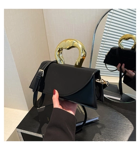 Detail of elegant black square bag with artistic gold ring handle and matte finish