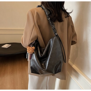 Detail of a black soft leather shoulder bag with a wide pleated strap and a cute bear charm
