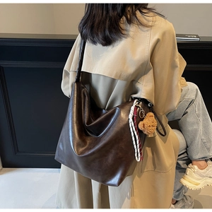 Detail of dark brown faux leather tote bag with a plush bear charm on a beige trench coat