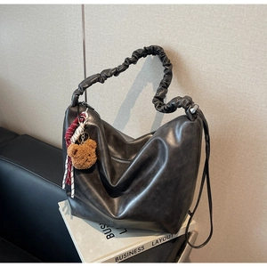 Detail of dark grey leather hobo bag with scrunchie handle and plush bear charm