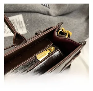 Details einer dunkelbraunen Lackledertasche mit goldenem Reißverschluss und Logo
