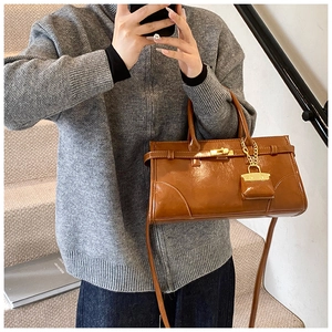 Detail einer karamellbraunen Ledertasche mit goldenem Drehverschluss und Minianhänger
