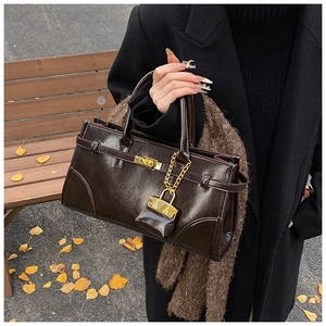 Detail einer dunkelbraunen Lackleder-Handtasche mit Metallschloss und Mini-Anhänger
