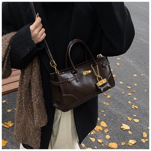 Detail of a dark brown glossy leather handbag with gold lock in an autumn street setting