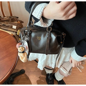Detail of black leather Boston bag with gold PAN TOR logo and cute bear charm pendant