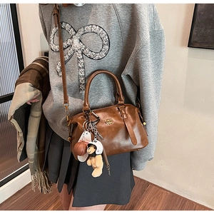 Close-up of brown leather baseball bag featuring plush bear and basketball charms