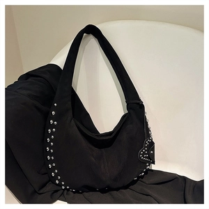 Détail d'un sac à bandoulière noir mat avec clous argentés et breloque en forme de cœur