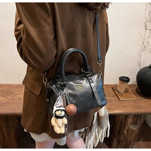 Black leather Boston bag with plush bear charm and mini basketball on a crossbody strap