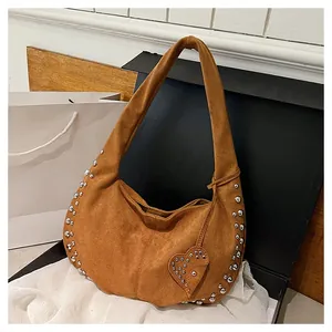 Détail de l'écusson en cœur avec clous argentés sur sac demi-lune en daim marron mat