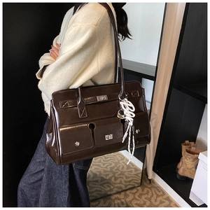 Detail of dark brown glossy leather messenger bag with metal locks and woven tassel