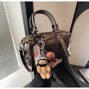 Detail of dark brown vintage bowling bag with bear charm and golden logo on leather
