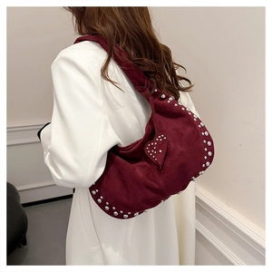 Détail d'un sac sous le bras en daim bordeaux mat avec des clous et une breloque en cœur