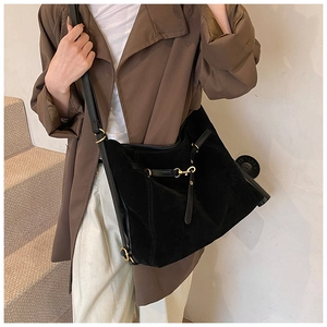 Detail of black suede tote bag with golden metal buckles on a neutral staircase background