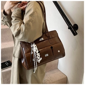 Detail of a brown glossy shoulder bag featuring silver locks and a white letter pendant