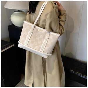 Detail of plush beige tote bag showing texture, metal logo and slim leather straps