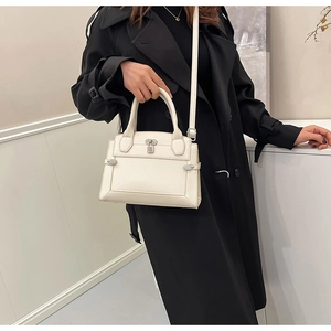 Close-up of cream lychee leather handbag with silver lock worn on a black trench coat