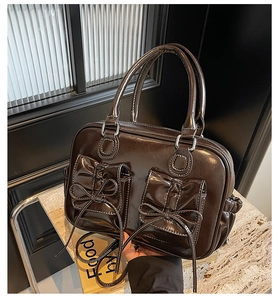 Detail of dark brown glossy handbag featuring dual front pockets with bow ties and handles