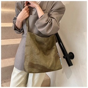 Detail of dark green canvas tote bag with side label on shoulder of a model