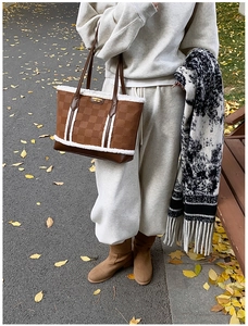 Detail of caramel checkerboard tote bag with plush trim and gold logo in autumn setting