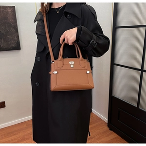 Detail of a brown leather satchel featuring a silver lock and cross-body strap