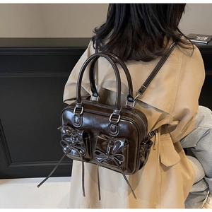 Deep brown glossy patent leather backpack with bow details shown on a model