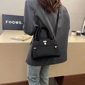 Sac à main trapèze noir en cuir grainé avec fermoir argenté porté dans un décor urbain