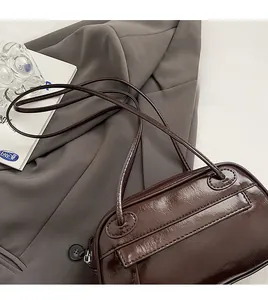 Detail of dark brown glossy patent leather shoulder bag with wrinkled texture on grey fabric