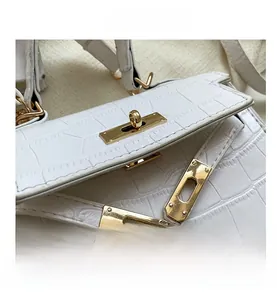 Detailed close-up of golden metal twist lock on white crocodile pattern handbag