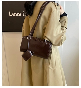 Detail view of a glossy dark brown tote bag with a small coin purse pendant on a trench coat