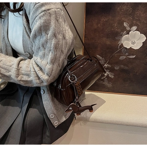 Detail of dark brown patent leather shoulder bag with cute dachshund charm and accessories