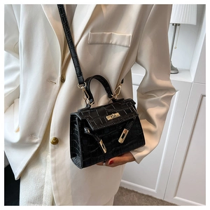 Detail of black crocodile pattern leather texture and golden metal lock on Kelly bag