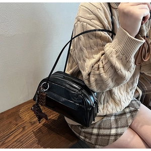 Detail of glossy black PU shoulder bag with triple zippers and cute decorative pendants
