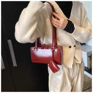 Detail of dark red glossy tote bag with mini charm pouch shown on white cardigan