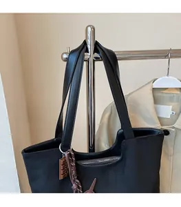 Détail du sac cabas noir avec de larges bandoulières robustes et un pendentif chocolaté