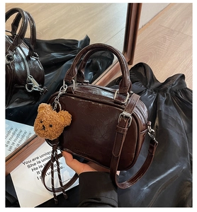 Detail of dark brown glossy Boston bag with detachable strap and cute bear charm