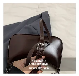 Detail of adjustable shoulder strap and silver metal buckle on dark brown glossy bag