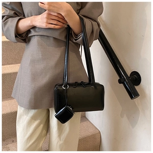 Side view of black faux leather shoulder bag with a mini charm pouch on a staircase