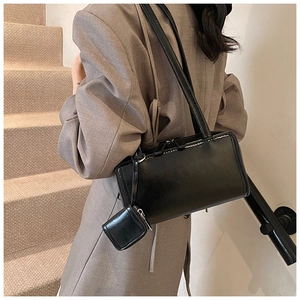Minimalist black rectangle shoulder bag with detachable mini pouch on a grey suit model