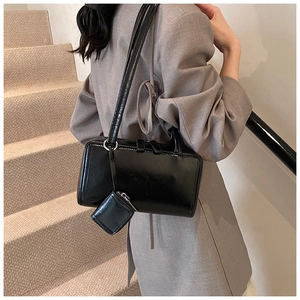 Detail of glossy black shoulder bag with a small zip pouch and silver hardware on model