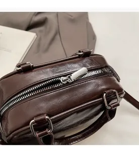 Close-up of a dark brown oil wax leather handbag with silver zipper and buckle detail