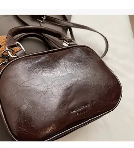 Detailed close-up of dark brown oily leather texture with embossed brand logo on a retro bag