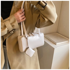 Close-up of cream rectangular tote bag with matching mini charm on model shoulder