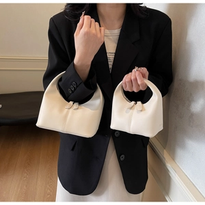 Comparison of two sizes of cream minimalist leather handbags shown by a fashion model