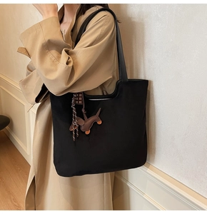 Détail d'un grand sac cabas noir avec une breloque de sac en forme de chien en cuir brun