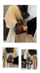 Detail of a brown polished leather Boston bag featuring a plush bear charm and shoulder strap