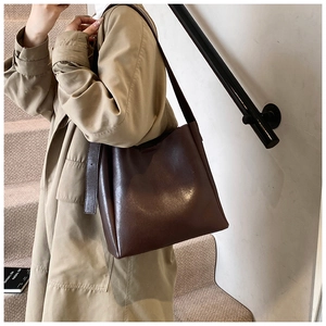 Detail of a dark brown leather bucket bag on shoulder of a model in a trench coat