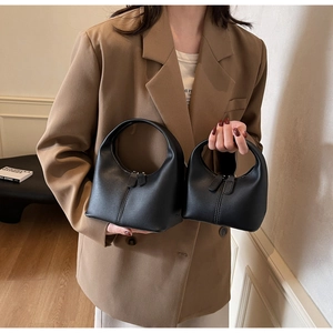 Detail view of large and small black crescent hobo bags with circular handles on a bench