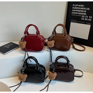 Close-up of four colors of glossy leather Boston bags with plush bear charms on display