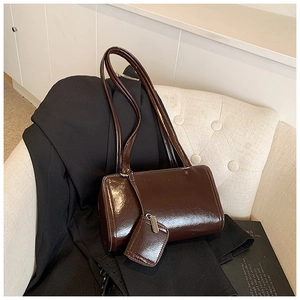 Close-up of deep brown oil wax leather tote bag with mini charm on a fabric sofa