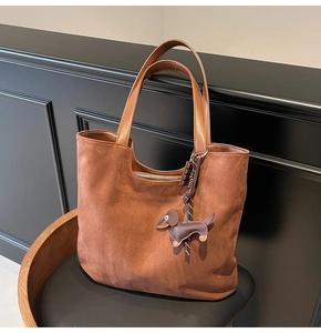 Détail d'un sac cabas en daim marron avec un pendentif charmant en cuir en forme de teckel
